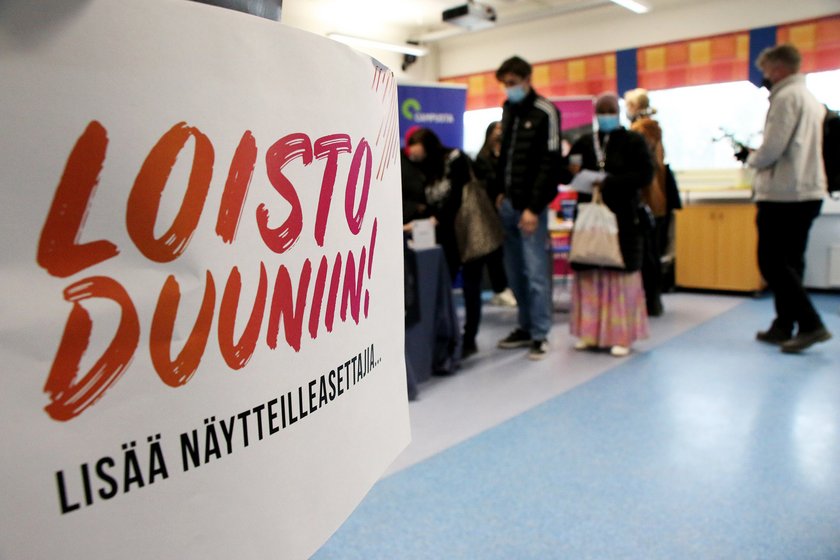 Vasemmalla Loistoduuniin-kyltti, oikealla taustalla ihmisiä työnhaussa luokkahuoneessa.